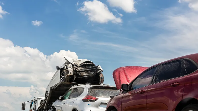 A heavily wrecked white car likely from a major accident is being loaded onto or piled on top of another white SUV.