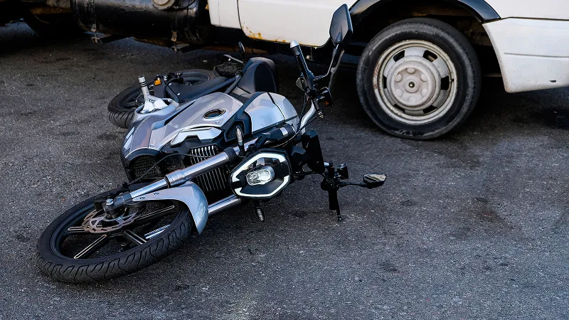 Silver motorcycle lying on asphalt near four wheel vehicle after road crash.
