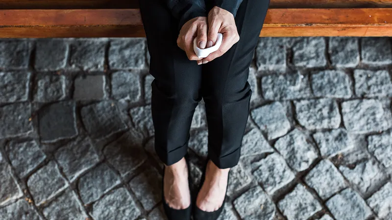 Overhead view of woman wearing all black and holding handkerchief while sitting on bench.